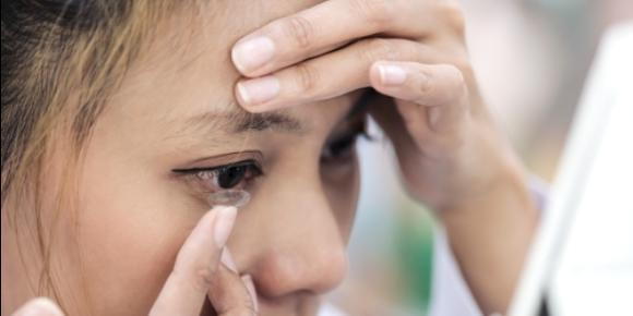 A woman inserting contact lenses while looking in a mirror