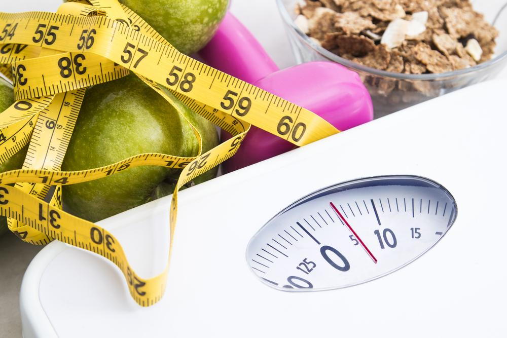 scale with measuring tape, dumbbell, apple, and granola