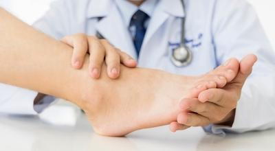 Doctor-in-coat-hold-and-massage-the-foot-of-patient.