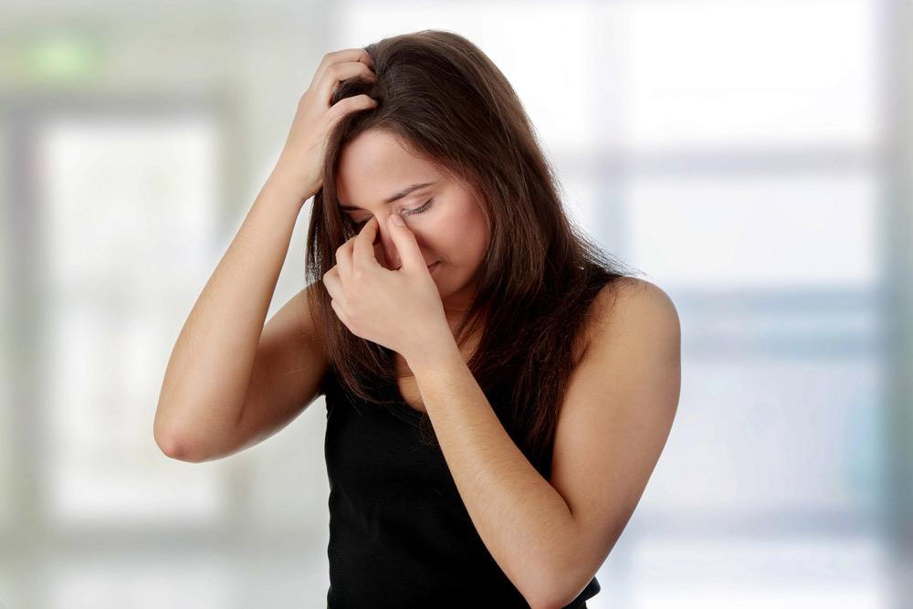 woman holding her head and nose