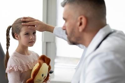 Doctor holding the young girl forehead for temperature on clinic