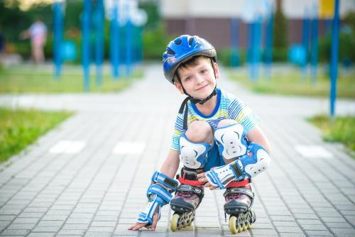 A child wearing a helmet, knee pads, and elbow pads while inline skating outdoors.