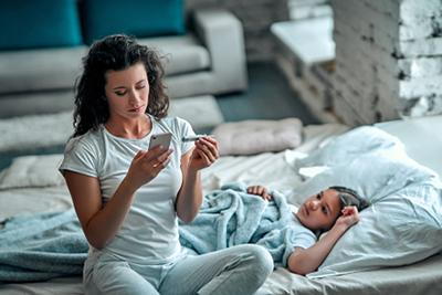 Mother-using-phone-to-call-holding-thermometer-with-sick-child