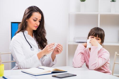 Pediatrician monitoring a child's temperature caused by flu symptoms.