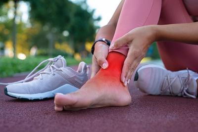 Woman-runner-holding-her-ankle-in-pain-with-red-highlights-outdoor.