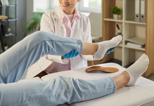 A podiatrist fitting a custom orthotic in a patient's shoe or foot.