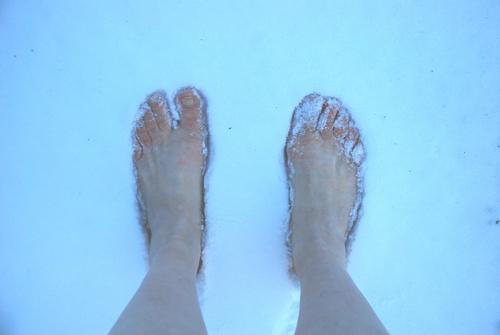 Bare feet of a man standing on snow with frostbite risk