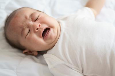 Illustration of newborn baby in bed and crying.