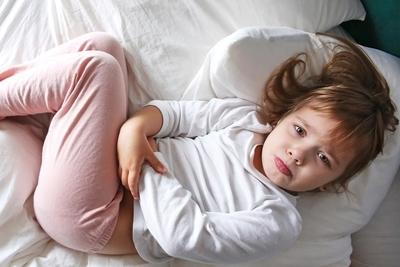 Young girl on bed suffering from abdominal pain while lying on bed