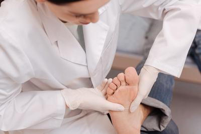 Doctor in gloves checking sole of patient’s foot during podiatry visit