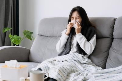 Young woman sneezning while sitting on sofa