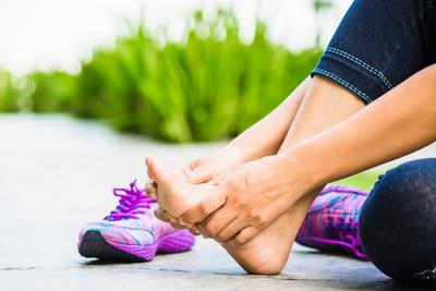 Woman-holding-her-Arch-in-pain-with-purple-shoes-beside-the-road.