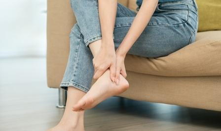 Heel pain from a woman in jeans while sitting on sofa.