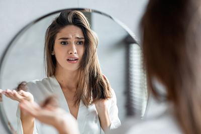 Female hair shedding shown by woman holding fallen hair with distressed expression