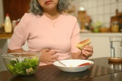 Woman clutching stomach holding sandwich in kitchen