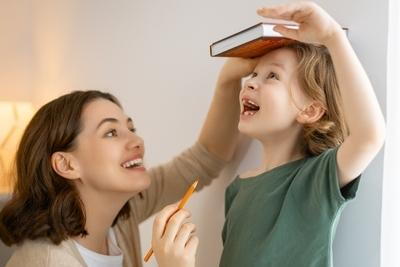 Happy-mom-measures-the-child's-height-with-a-book