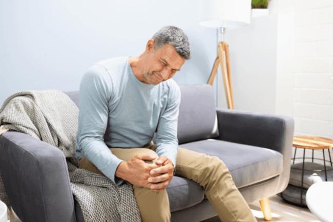 Old man sitting on the couch feeling of intense pain caused by Arthritis or Osteoarthritis