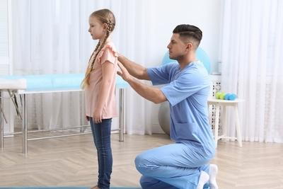 Young girl in the clinic with the doctor checking her back.