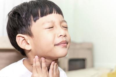 Young boy feeling hurt holding his neck from sore throat