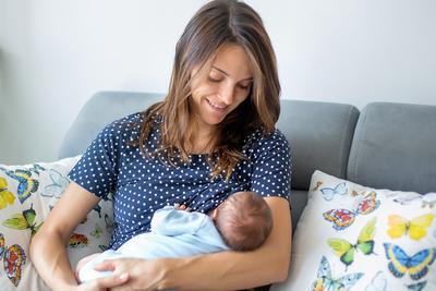 Mother taking care and feeding her baby on sofa