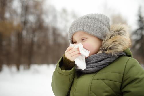 Young boy wiping his nose outdoors during winter