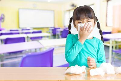 Girl with cold symptoms using tissue at school