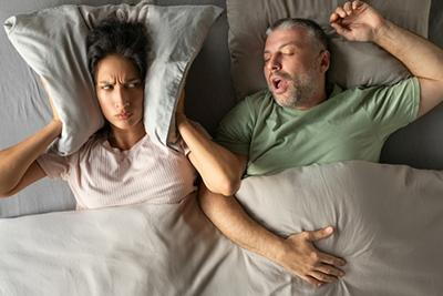 Tired woman struggling to sleep due to loud snoring from partner