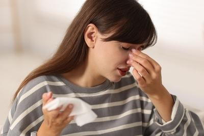 Young woman touching nose with tissue, appearing to have sinusitis symptoms