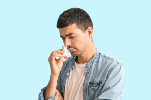 Man managing nosebleed with tissue against blue backdrop