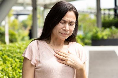 Woman-outdoors-holding-chest-wincing-in-discomfort
