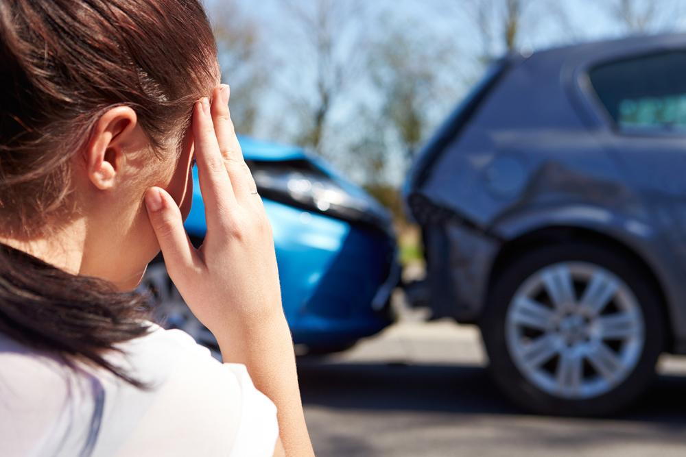 Woman holding her head in pain from an auto accident injury with a car accident in background