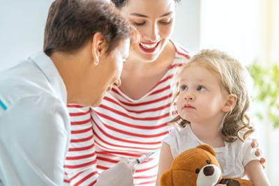 Doctor having a vaccination to a young girl with her mother beside her