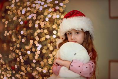 Child feeling overwhelmed while hugging a teddy bear at holiday time.