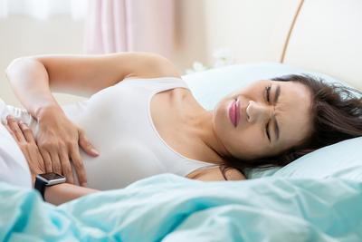 Young woman lying in bed holding stomach in pain