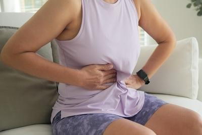 Person holding abdomen while sitting on couch with digestive discomfort