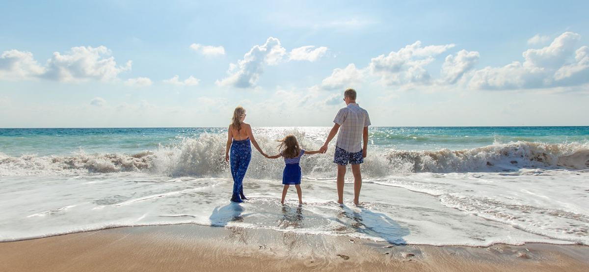 mother and father holding daughter's hands on beach
