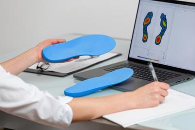 Podiatrist checking the balance and condtion of foot orthotics on laptop