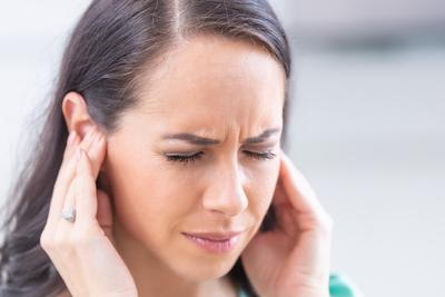 Woman with closed eyes holding ears in discomfort
