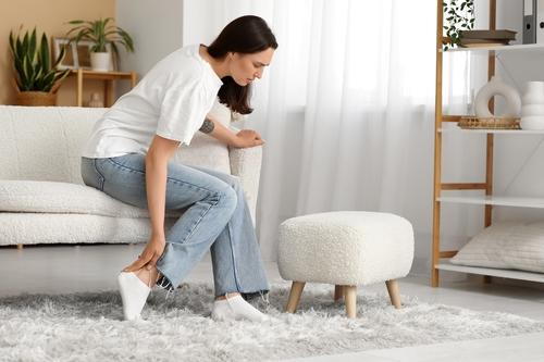 Woman holding her foot due to posterior tibial tendon dysfunction at home