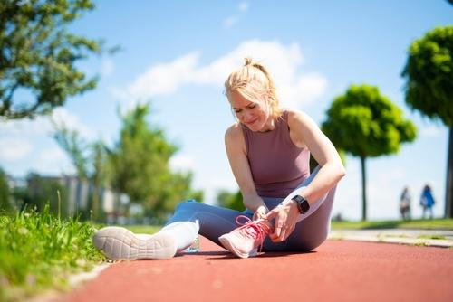 Woman holding her ankle outdoors, experiencing pain caused by arthritis.