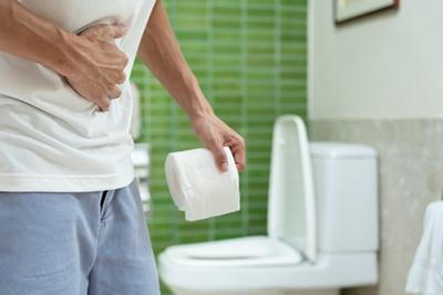 Adult man clutching his abdomen and holding toilet paper, experiencing diarrhea and stomach discomfort.