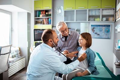 Elderly man visiting doctor with grandchild for routine checkup