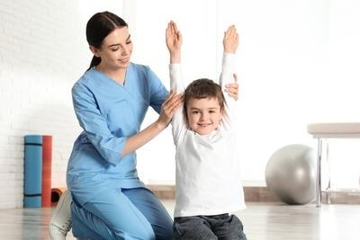 Clinical assistant stretching the arms of a little boy on clinic.