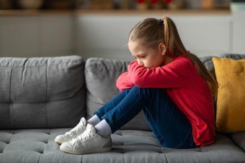 Sad-Young-Girl-in-red-Sweater-Hugging-Knees-on-Couch.