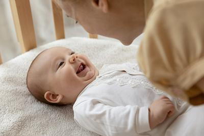 Smiling baby playing with mother in crib.