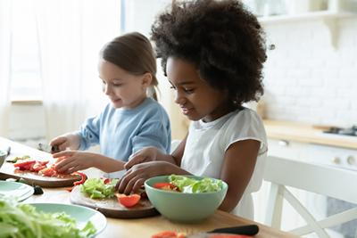 Young girls happily slice the food in the kitchen.