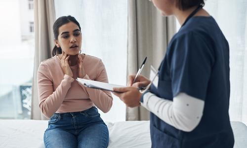 Woman discussing chronic sore throat symptoms with ENT medical assistant before consultation.