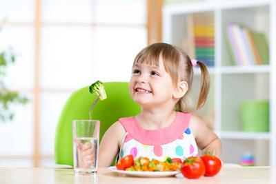 Little-girl-smiling-holding-a-broccoli-in-fork-and-tomatoes-in-plate.