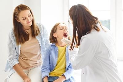 Doctor checking the throat of a young girl with her mother