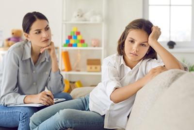 A-mother-attentively-listens-to-her-upset-daughter-on-a-couch.